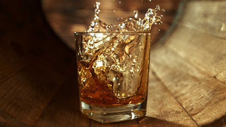 A drink being poured into a whisky tumbler, and splashing back out of the glass